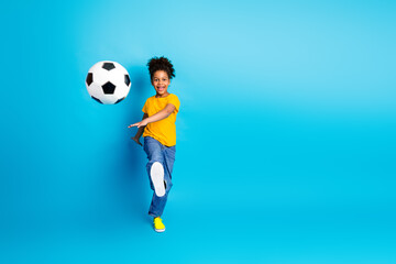 Young girl playing with a soccer ball while wearing casual attire on a bright blue background