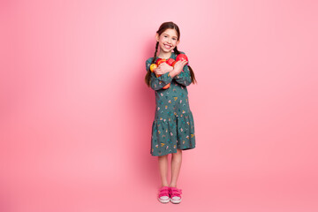 Adorable young girl holding apples with a joyful smile, standing against a vibrant pink studio...