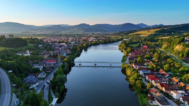 Flight over the river approaching the bridge over it. Lovely rural area located on the banks of the river at sunset. Countryside in Slovakia.
