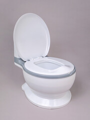 White with gray stripe children's plastic potty in the form of a toilet with an open lid on a gray background