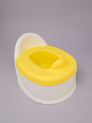 White baby potty with yellow lid on grey background