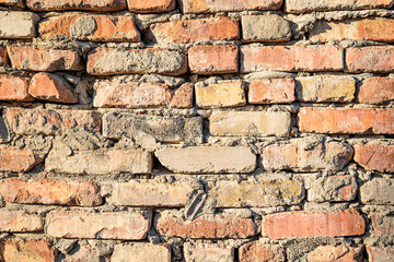 Close-up of an old, weathered brick wall with rough mortar in warm sunlight, showcasing texture and...
