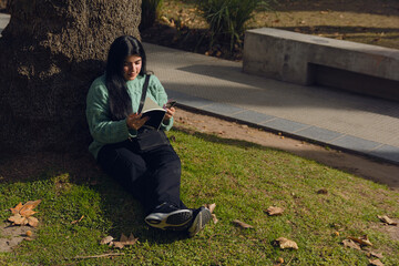 young calm woman reading in the park sitting leaning against a tree