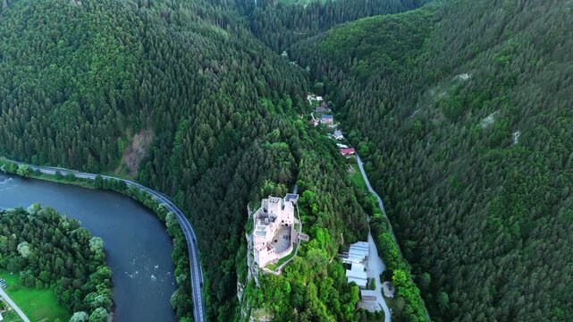 Beautiful castle on the mountain top over the river flowing at the foot. Drone footage above verdant Tatra Mountains covered with evergreen woods. Slovakia.
