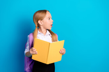 Portrait of a young schoolgirl holding a yellow book against a blue background, dressed in a...