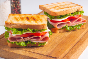 Close-up of two sandwiches with bacon, salami, prosciutto and fresh vegetables on rustic wooden...