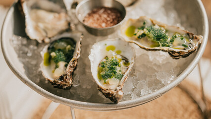 A plate of oysters with a green sauce on top. The plate is on a table with a white background