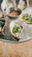 A plate of oysters with a green sauce on top. The plate is on a table with a silver tray