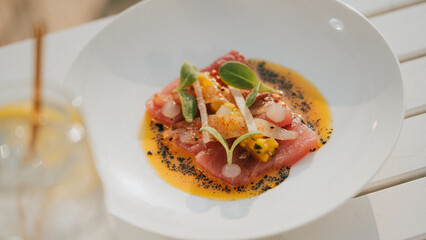 A plate of food with a sauce and a garnish on top. The plate is white and the food is pink