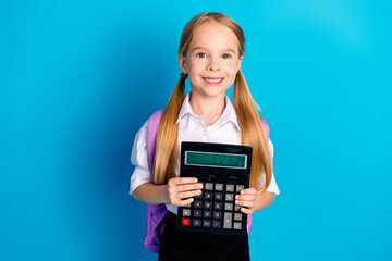 Smiling female student holding a large calculator against a bright blue background with ponytails...