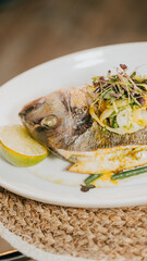 A plate of fish with a lime wedge on it. The fish is garnished with green vegetables