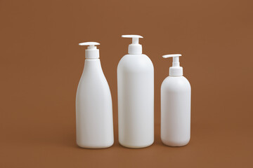 three white bottles containers with dispensers on brown background, mock up for products copy space