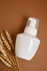 wheat and white mock up bottle with dispenser on brown background, natural cosmetic product