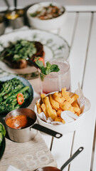 A table with a variety of food and drinks, including a bowl of fries and a glass of pink lemonade