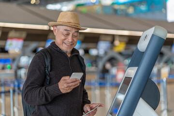asian senior man passenger using smartphone,doing self check in at self service check in machine or KIOSK at the airport terminal,elderly retired with modern lifestyle,technology,transportation,travel