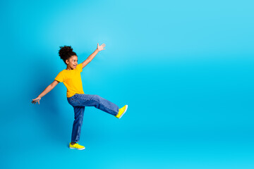 Fototapeta premium Cheerful young girl in casual outfit expressing joy against a vibrant blue background in a studio setting