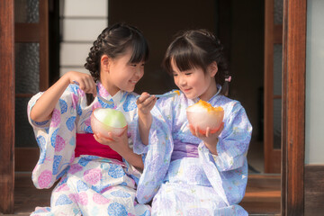 縁側でかき氷を食べる浴衣姿の姉妹