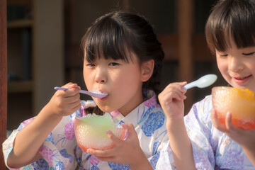 縁側でかき氷を食べる浴衣姿の姉妹