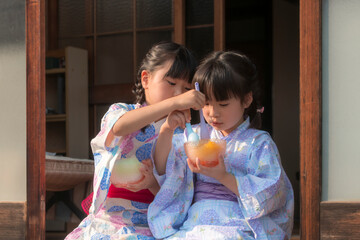 縁側でかき氷を食べる浴衣姿の姉妹
