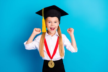 Cute schoolgirl celebrating academic achievements in graduation cap with medal on a vibrant blue...