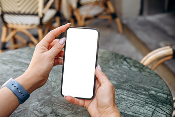 Mockup woman's hand holding using smart phone with white blank screen POV at coffee shop, mobile...