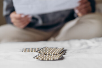 woman holding a glass of water in one hand and a variety of colorful capsules in the other, preparing to take medication, showcasing health and wellness routine in a cozy indoor setting