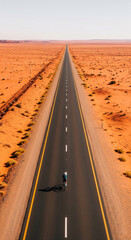 Fototapeta premium Aerial view of cyclist on long desert road, showcasing journey, freedom, and adventure in vast landscape