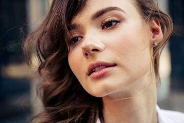 Fototapeta premium Charming young woman with brunette hair looking into distance during sunny day in urban street environment