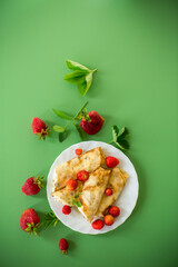 Plate with pancakes and fresh strawberries on a green background