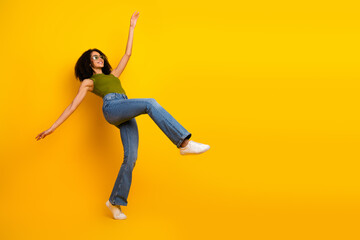 Young stylish woman in green top and jeans on yellow background, showcasing casual fashion, curly...
