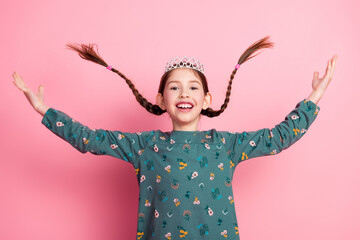 Happy young girl with braided hair wearing a tiara smiling with excitement against a vibrant pink background © deagreez
