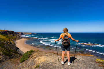 Beautiful mature woman hiker standing on cliff at viewpoint on Atlantic ocean on sunny and windy...