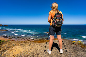 Beautiful mature woman hiker standing on cliff at viewpoint on Atlantic ocean on sunny and windy...