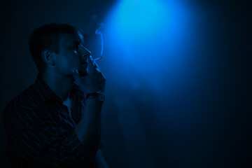 Moody portrait of a man smoking in blue dramatic lighting. The scene is atmospheric and cinematic,...