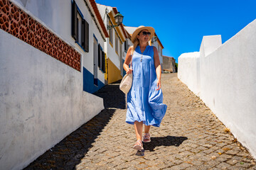 Beautiful middle aged woman tourist walking downhill narrow street in portuguese town on sunny...