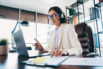 Professional businesswoman working in an office, speaking through a headset while using a laptop...