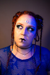 Futuristic woman with bold makeup, glowing blue eyes, circuit patterns on her face, braided hair with glitter, and blue mesh top in sci-fi inspired style.