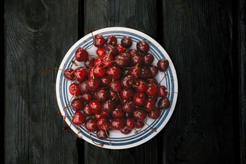 A vibrant image of ripe cherries on a plate set against a dark wooden backdrop. A plate of fresh, juicy cherries sits on a rustic black wooden table, capturing a vibrant, appetizing scene.