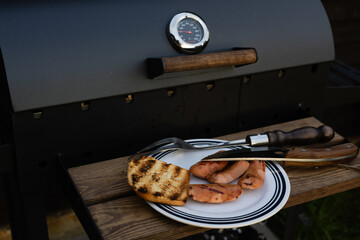 A delicious grilled meal featuring sausages and toast is ready for the summer season. A barbecue grill with food on a wooden surface, ready to be served. The scene is set outdoors on a sunny day.