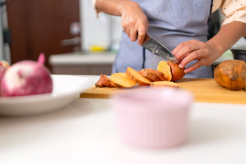 Chef slicing sweet potato on wooden cutting board in kitchen