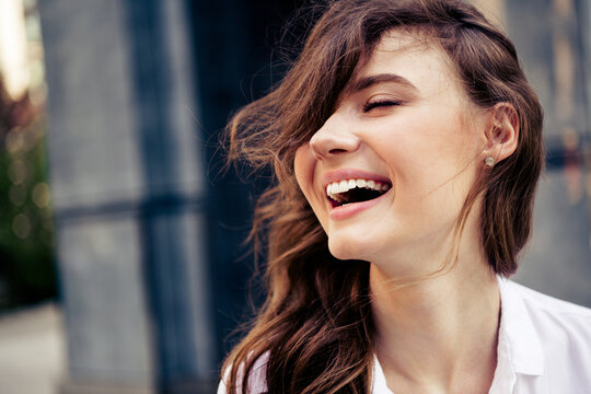 Young cheerful woman with flowing hair laughing outdoors in sunny urban setting during a casual spring day