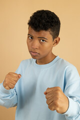 Vertical image of a dark skinned teenager wearing a light blue sweatshirt with both fists up ready...