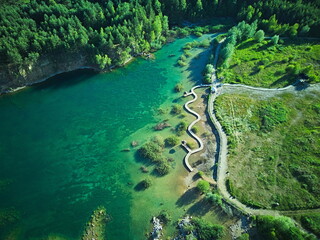 Aerial View of Serpentine Wooden Path Over Turquoise Lake and Forested Shoreline