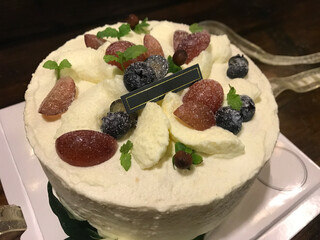 A round cream cake topped with fresh fruits (grapes, blueberries), mint leaves, and a blank black...