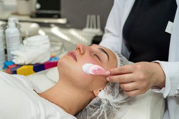 Beautician applies cleansing and moisturizing white cream with help of brush on client's face