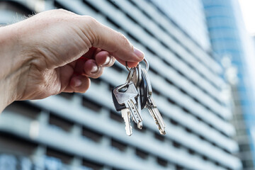 Close-Up of Hand Holding House Key in Front of Modern Apartment Building