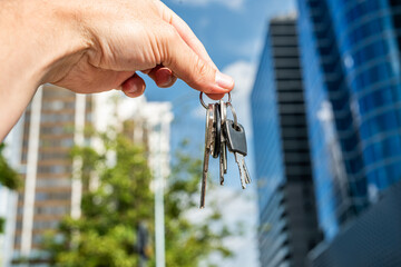 Keys in Hand Against Modern Office Skyscrapers – Real Estate and Investment Concept.  Perfect for business  real estate finance and architecture-related visuals.