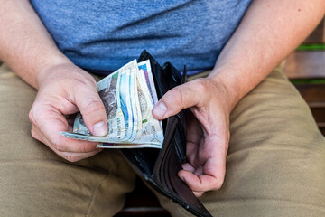 Counting Polish Zloty – Hands of a Man with Wallet and Cash.  A man in casual clothes holding and counting Polish zloty notes from a black leather wallet.