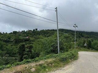 Misty rural hillside with lush green vegetation, scattered houses, and a winding dirt road under a...