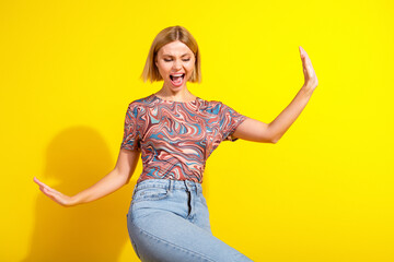 Energy and happiness of a young blonde woman in vibrant casual outfit standing against a yellow...